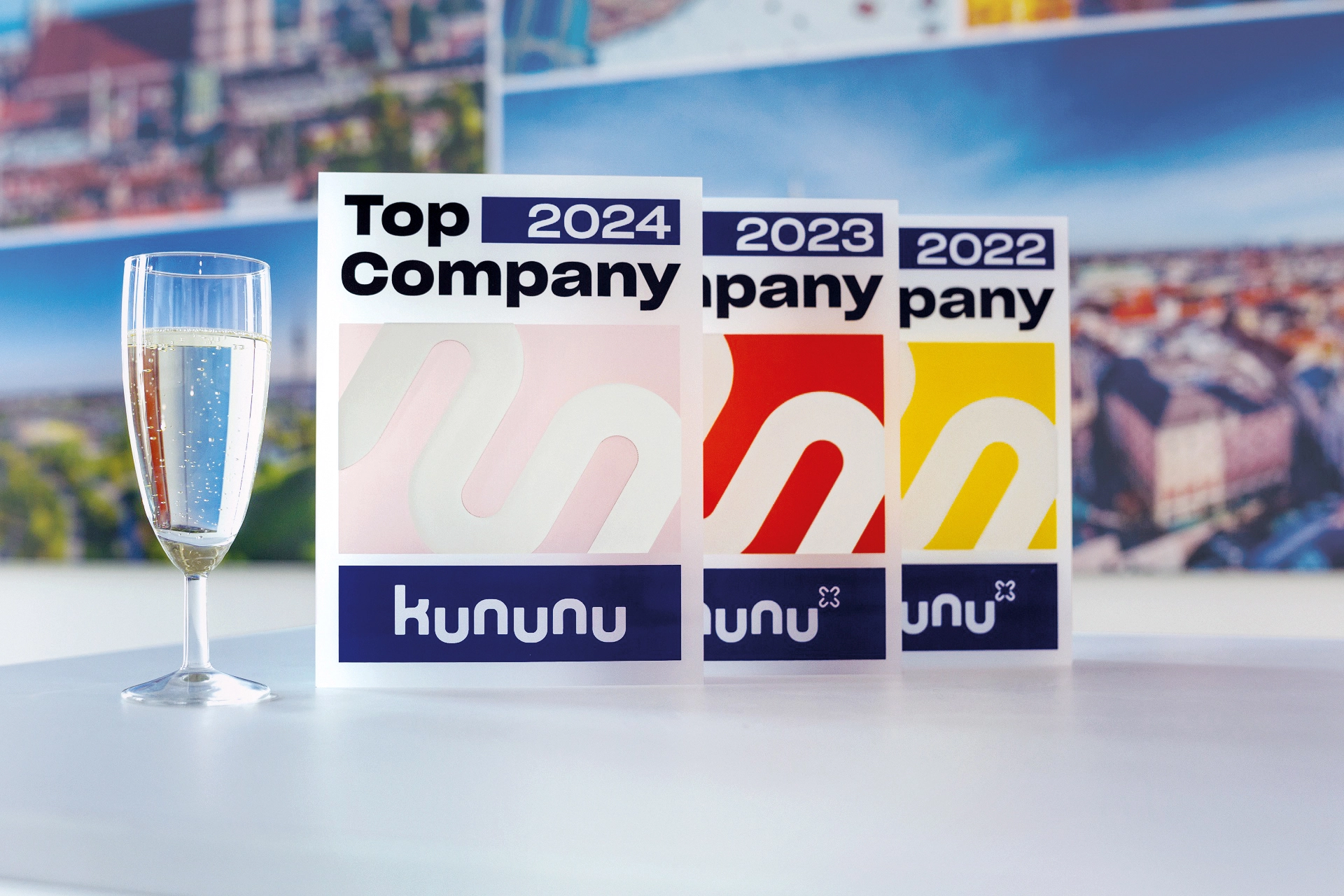 Amadeus Fire Kununu Top Company Award 2024, 2023 und 2022, neben einem Champagne Glass