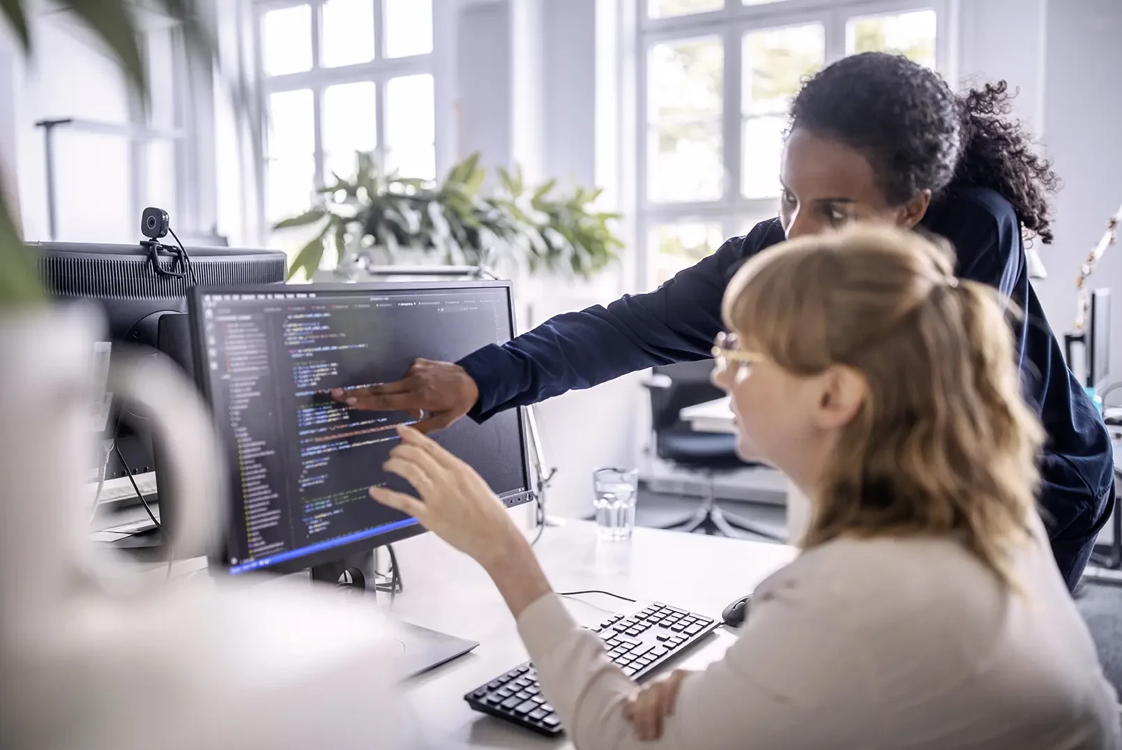 Eine Arbeitskollegin zeigt der anderen etwas auf dem PC Bildschirm