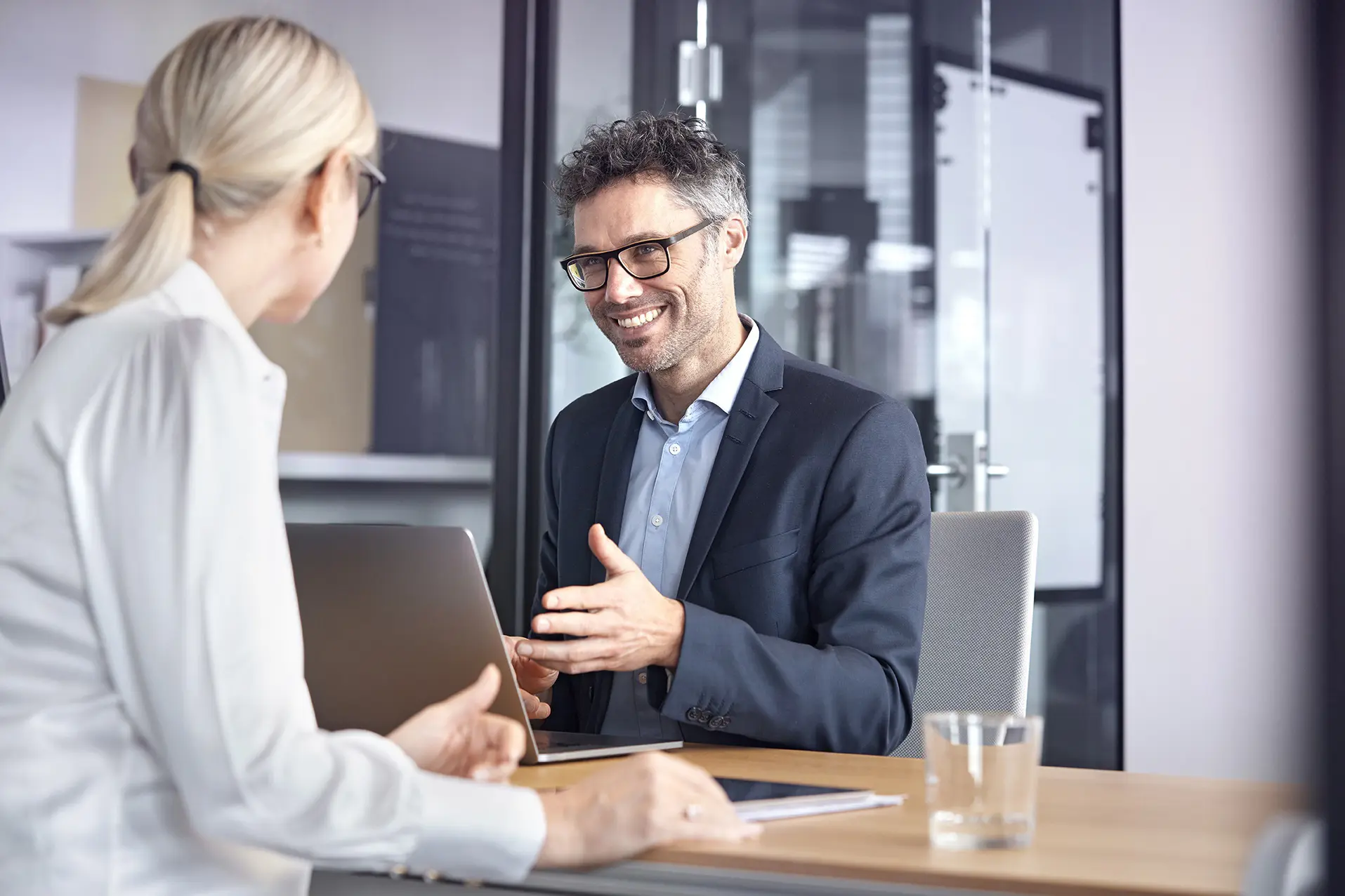 Ein Business Mann mit Brille und Sakko unterhält sich mit einer Frau