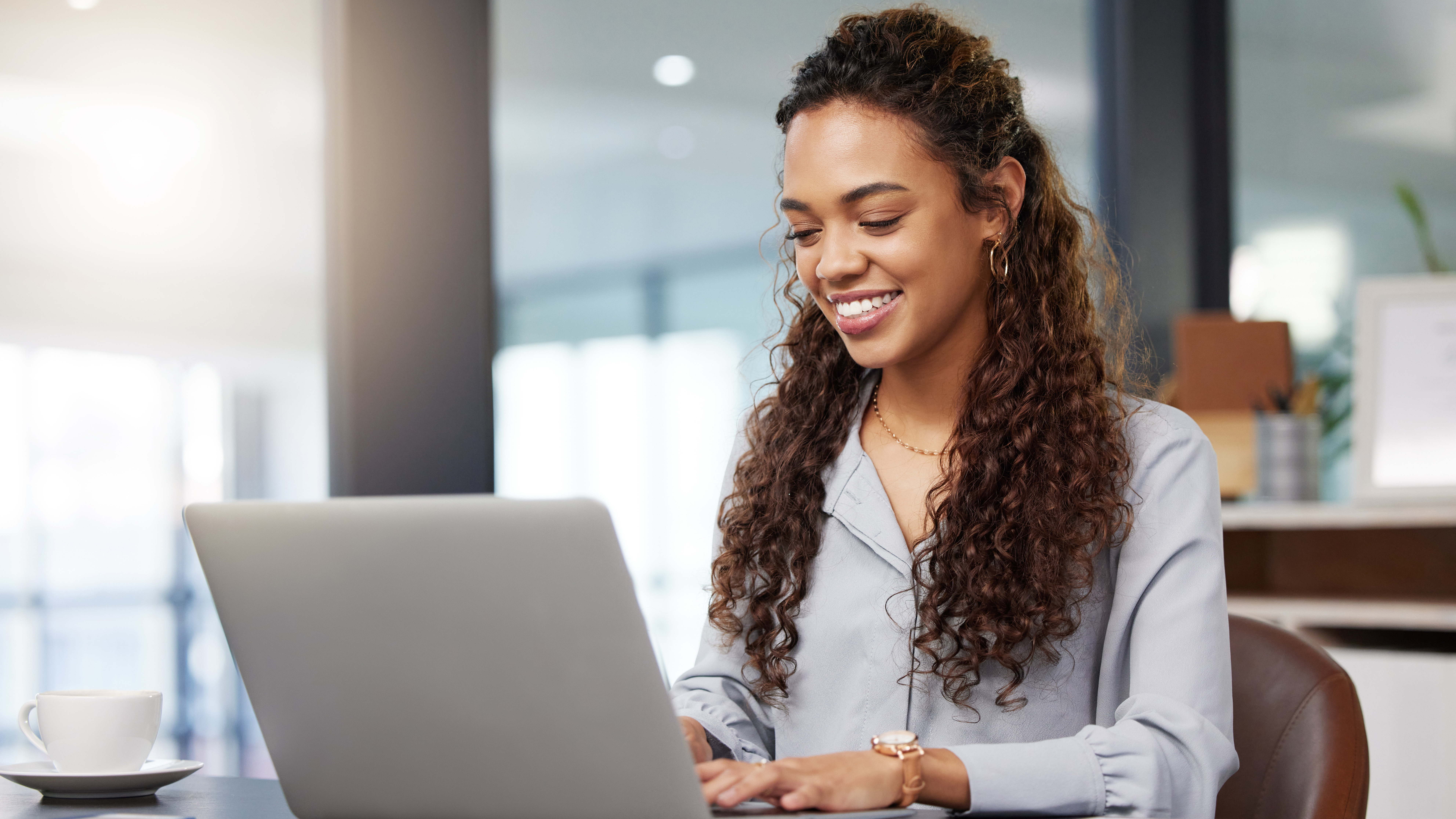 Eine junge Frau schaut lächelnd auf Ihrem Laptop und schreibt ihr Bewerbungsschreiben